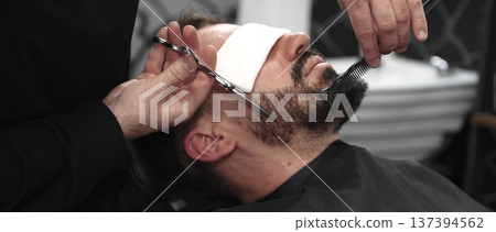 Professional barber carefully trimming beard with scissors, creating clean lines and sharp detailing inside contemporary barbershop workspace Professional barber carefully trimming beard with scissors, creating clean lines and sharp detailing inside contemporary barbershop workspace 137394562