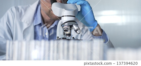 Male scientist researcher wearing blue gloves, protective glasses is using microscope in modern laboratory, portrait view. Low key lighting photo. Science and Medicine concepts 137394620
