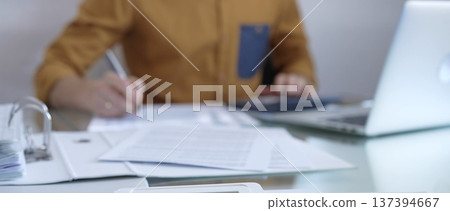 Magnifying glass, calculator, pen and documents are lying on accountant's desk. Businessman or accountant, wearing yellow shirt, is working with documents on the background. Business people, audit 137394667