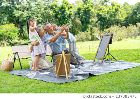 Asian senior man and woman action of selfie the picture together with two little girls during relax with family in the public park together with day light. Asian senior man and woman action of selfie the picture together with two little girls during relax with family in the public park together with day light. 137395473