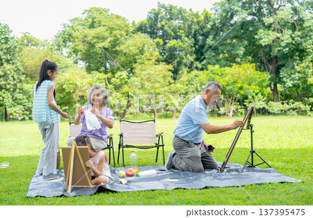 Senior man try to help add or support by drawing on board of the girl during relax with family in public park. Senior man try to help add or support by drawing on board of the girl during relax with family in public park. 137395475