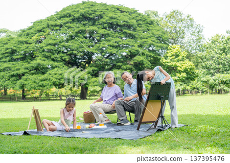 The Asian girl stand and look at her paint or drawing and she look happy with senior man and woman glad the performance in the back during family relax at public park. The Asian girl stand and look at her paint or drawing and she look happy with senior man and woman glad the performance in the back during family relax at public park. 137395476