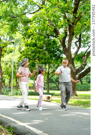 Vertical image of Asian senior man and woman also the girl action of stretching the waist and they look happy in public park together Vertical image of Asian senior man and woman also the girl action of stretching the waist and they look happy in public park together 137395482