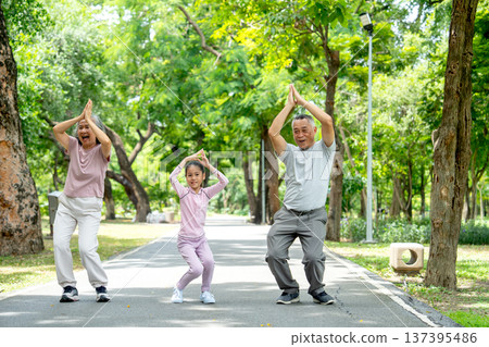 Asian senior man and woman also the girl action of stretching the waist and knees and they look happy in public park together. 137395486