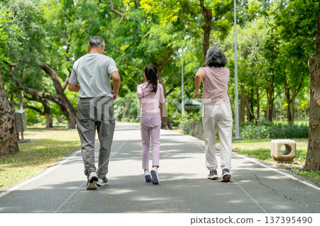 Back of Asian girl run along with senior man and woman in the public park and they look happiness that have good time together. Back of Asian girl run along with senior man and woman in the public park and they look happiness that have good time together. 137395490