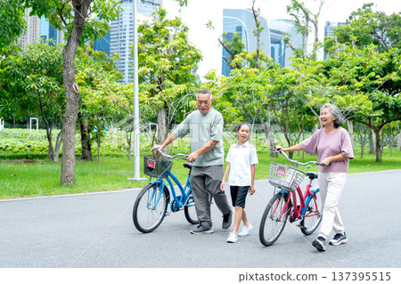 Side view of senior man and woman leading the bicycles with the girl who walk on the road together in the public park with day light. 137395515