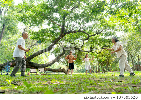 Asian senior man and woman enjoy to play badminton in public park with happiness and two little girls cheer up beside. Asian senior man and woman enjoy to play badminton in public park with happiness and two little girls cheer up beside. 137395526