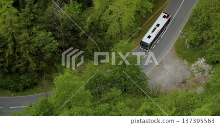 Bus travels along winding road surrounded by green trees in a rural area during daytime Bus travels along winding road surrounded by green trees in a rural area during daytime 137395563
