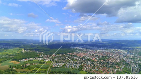 View of a large town surrounded by fields and hills under a blue sky with clouds in the distance during daytime View of a large town surrounded by fields and hills under a blue sky with clouds in the distance during daytime 137395616