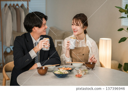一對年輕的亞洲夫婦正在家裡的餐桌上吃喝。 137396946