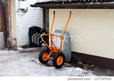Weathered hand cart in snowy alleyway. Old industrial trolley rests against chipped brick wall Weathered hand cart in snowy alleyway. Old industrial trolley rests against chipped brick wall 137397916