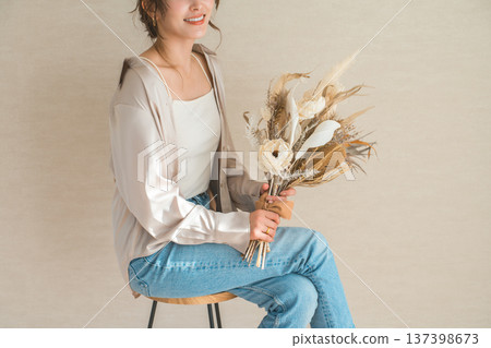 一位身穿時尚牛仔服的女模特兒坐在椅子上,手捧一束花。 一位身穿時尚牛仔服的女模特兒坐在椅子上,手捧一束花。 137398673