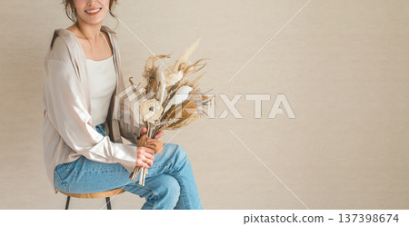 一位身穿時尚牛仔服的女模特兒坐在椅子上，手捧一束花。 137398674