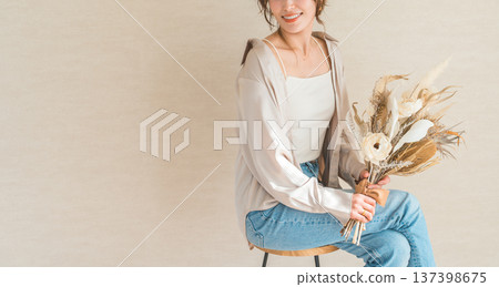 一位身穿時尚牛仔服的女模特兒坐在椅子上，手捧一束花。 137398675