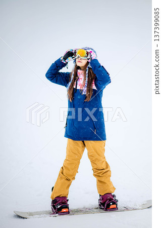 Young woman enjoying winter sports snowboarding on the slopes of a ski resort Young woman enjoying winter sports snowboarding on the slopes of a ski resort 137399085