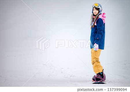 年輕女子在滑雪勝地的山坡上享受冬季運動-單板滑雪。 年輕女子在滑雪勝地的山坡上享受冬季運動-單板滑雪。 137399094