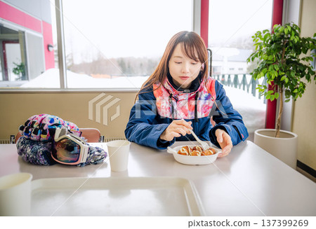 A young woman wearing ski wear eating a meal while taking a break 137399269