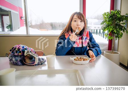 一位身穿滑雪服的年輕女子正在休息時用餐。 一位身穿滑雪服的年輕女子正在休息時用餐。 137399270