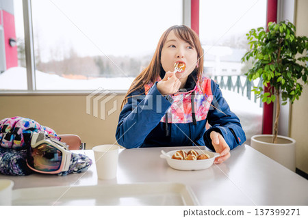 A young woman wearing ski wear eating a meal while taking a break A young woman wearing ski wear eating a meal while taking a break 137399271