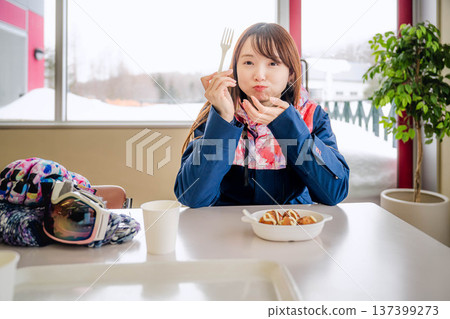 一位身穿滑雪服的年輕女子正在休息時用餐。 一位身穿滑雪服的年輕女子正在休息時用餐。 137399273