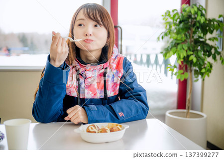 一位身穿滑雪服的年輕女子正在休息時用餐。 一位身穿滑雪服的年輕女子正在休息時用餐。 137399277