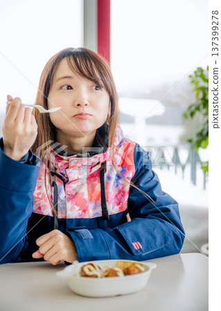 A young woman wearing ski wear eating a meal while taking a break A young woman wearing ski wear eating a meal while taking a break 137399278