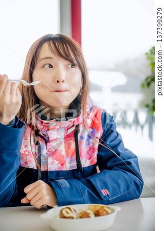 一位身穿滑雪服的年輕女子正在休息時用餐。 137399279