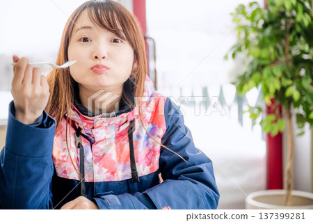 一位身穿滑雪服的年輕女子正在休息時用餐。 一位身穿滑雪服的年輕女子正在休息時用餐。 137399281