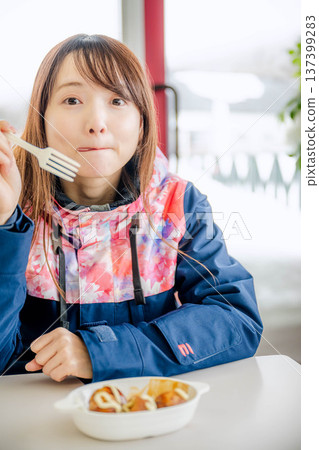 一位身穿滑雪服的年輕女子正在休息時用餐。 137399283