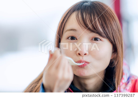 A young woman wearing ski wear eating a meal while taking a break A young woman wearing ski wear eating a meal while taking a break 137399287