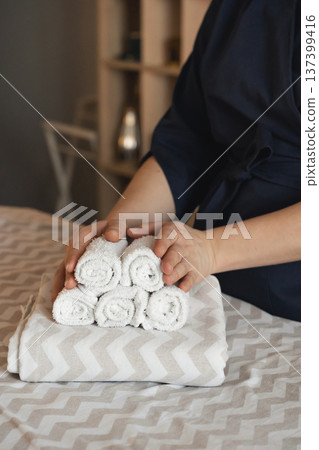 Spa therapist arranging clean, rolled white towels on a treatment bed, ready for a relaxing wellness or massage session 137399416