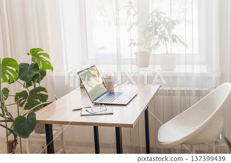 Bright minimalist home office with laptop on wooden desk, offering comfortable environment for remote work. Home office workspace Bright minimalist home office with laptop on wooden desk, offering comfortable environment for remote work. Home office workspace 137399439