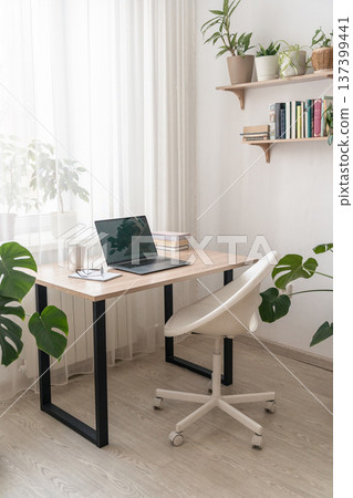 Minimalist study room featuring wooden desk, laptop, white ergonomic chair, green house plants, creating remote work environment 137399441