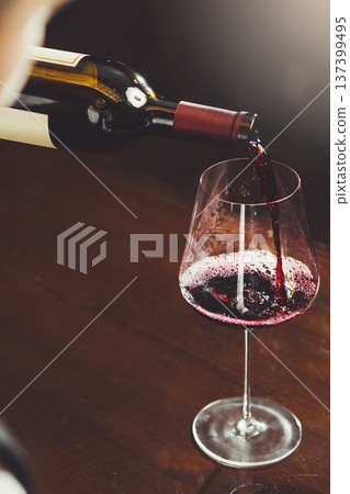 Close-up vertical image of bartender pours red wine to wineglass on bar counter background. Close-up vertical image of bartender pours red wine to wineglass on bar counter background. 137399495