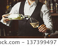 Sommelier pours white wine from a bottle into glass at the bar, close-up. 137399497