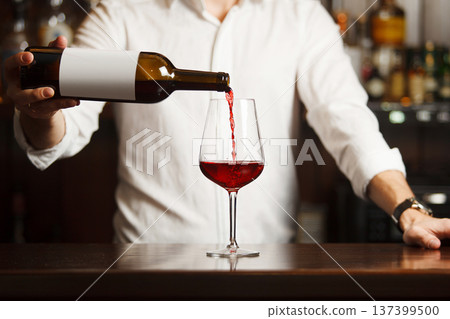 Male sommelier pouring red wine into long-stemmed wineglasses. Male sommelier pouring red wine into long-stemmed wineglasses. 137399500