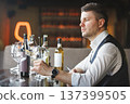 Sommelier sitting at table, looking at wineglass. 137399505