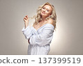 Senior female person in spa bathrobe has a perfectly clean healthy skin. Beautiful mature blonde woman wearing in housecoat over grey isolated background. 137399519