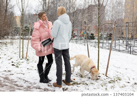 Two women interacting with dog outdoors in winter Two women interacting with dog outdoors in winter 137403104