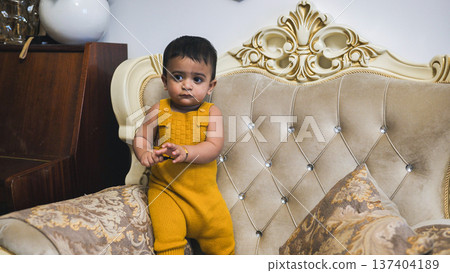 Cute baby boy in yellow romper standing on a traditional sofa at home Cute baby boy in yellow romper standing on a traditional sofa at home 137404189