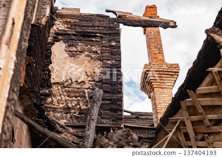 Structure of a burnt house revealing charred wood, brick chimney against cloudy sky Structure of a burnt house revealing charred wood, brick chimney against cloudy sky 137404193