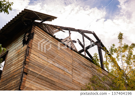 Burnt wooden house with destroyed roof showing fire damage and abandonment 137404196