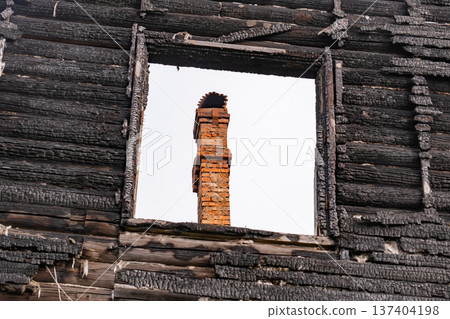 Charred log house wall with brick chimney seen through a window frame Charred log house wall with brick chimney seen through a window frame 137404198