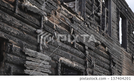 Facade of a burnt wooden building showing charred timber and empty windows after a fire. Facade of a burnt wooden building showing charred timber and empty windows after a fire. 137404201