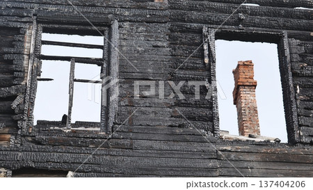 Charred wooden house exterior showing destruction and standing brick chimney Charred wooden house exterior showing destruction and standing brick chimney 137404206