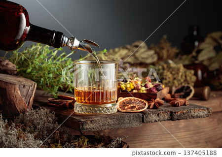 Herbal bitter liqueur is poured from a vintage bottle into a glass. Herbal bitter liqueur is poured from a vintage bottle into a glass. 137405188