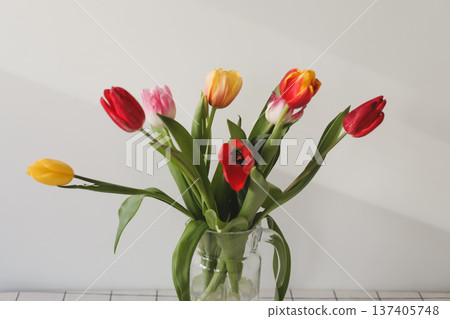 Fresh spring colorful bouquet of tulips in vase standing on white table in light classic design living room background. Festive flowers for gift. Mockup for greeting card Fresh spring colorful bouquet of tulips in vase standing on white table in light classic design living room background. Festive flowers for gift. Mockup for greeting card 137405748