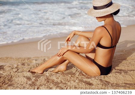 Woman applying sun cream lotion on legs. Skin cream.  A Female  smear  sunscreen on beautiful legs on beach. Sun protection 137406239