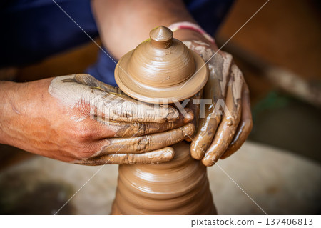 Skilled artisan hands shaping wet clay on a spinning potter wheel, creating a ceramic vase in a traditional pottery workshop. Skilled artisan hands shaping wet clay on a spinning potter wheel, creating a ceramic vase in a traditional pottery workshop. 137406813