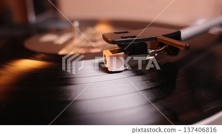 Macro view of record player cartridge and stylus tracking grooves on a spinning vinyl disc, warm bokeh background, concept of music, nostalgia and analog sound. Macro view of record player cartridge and stylus tracking grooves on a spinning vinyl disc, warm bokeh background, concept of music, nostalgia and analog sound. 137406816